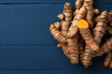 Pile of raw turmeric roots on blue wooden table, flat lay. Space for text