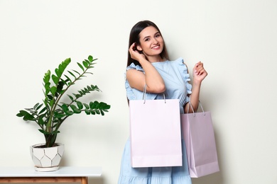 Photo of Beautiful young woman with blank paper bags near white wall, space for text