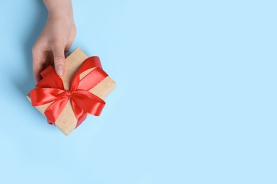 Photo of Woman holding gift box with red bow on light blue background, top view. Space for text