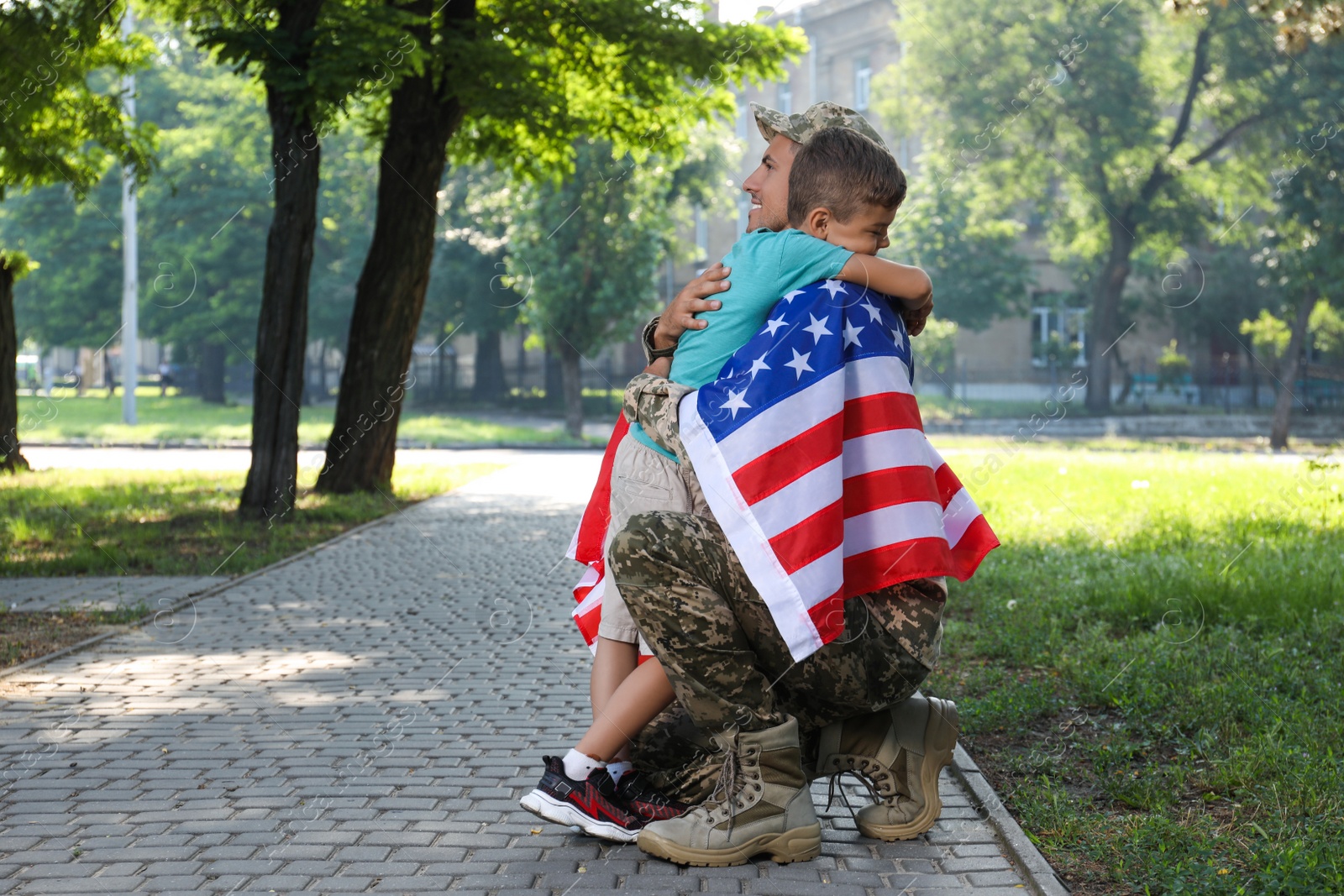 Photo of Soldier with flag of USA and his little son hugging outdoors