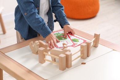 Little boy playing with set of wooden animals and fence at table indoors, closeup. Child's toy