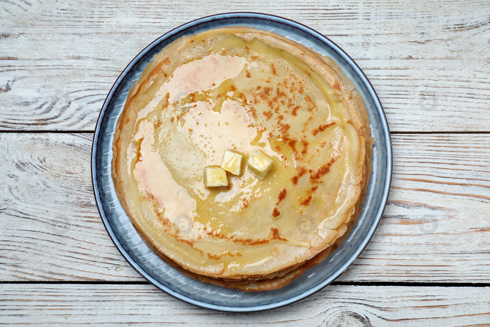 Photo of Delicious crepes with melting butter on white wooden table, top view