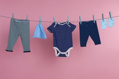 Photo of Different baby clothes drying on laundry line against pink background