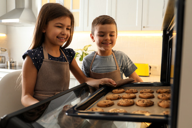 Photo of Cute little children taking cookies out of oven in kitchen. Cooking pastry
