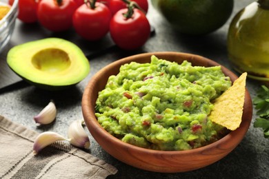 Photo of Delicious guacamole with nachos chips and ingredients on grey table, closeup