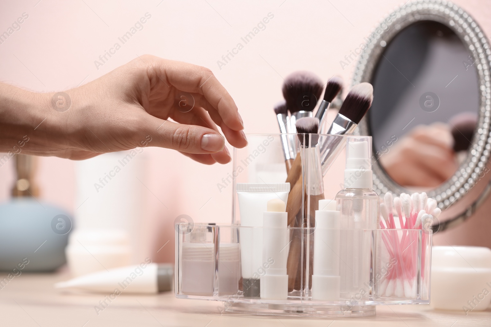 Photo of Woman taking cosmetic products from holder on dressing table, closeup