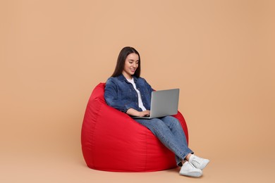 Photo of Smiling young woman working with laptop on beanbag chair against beige background, space for text