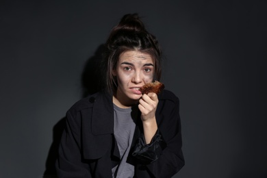 Photo of Poor woman with piece of bread on dark background