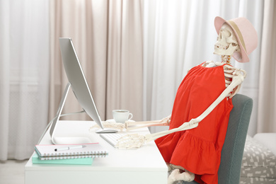 Photo of Human skeleton in red dress using computer indoors
