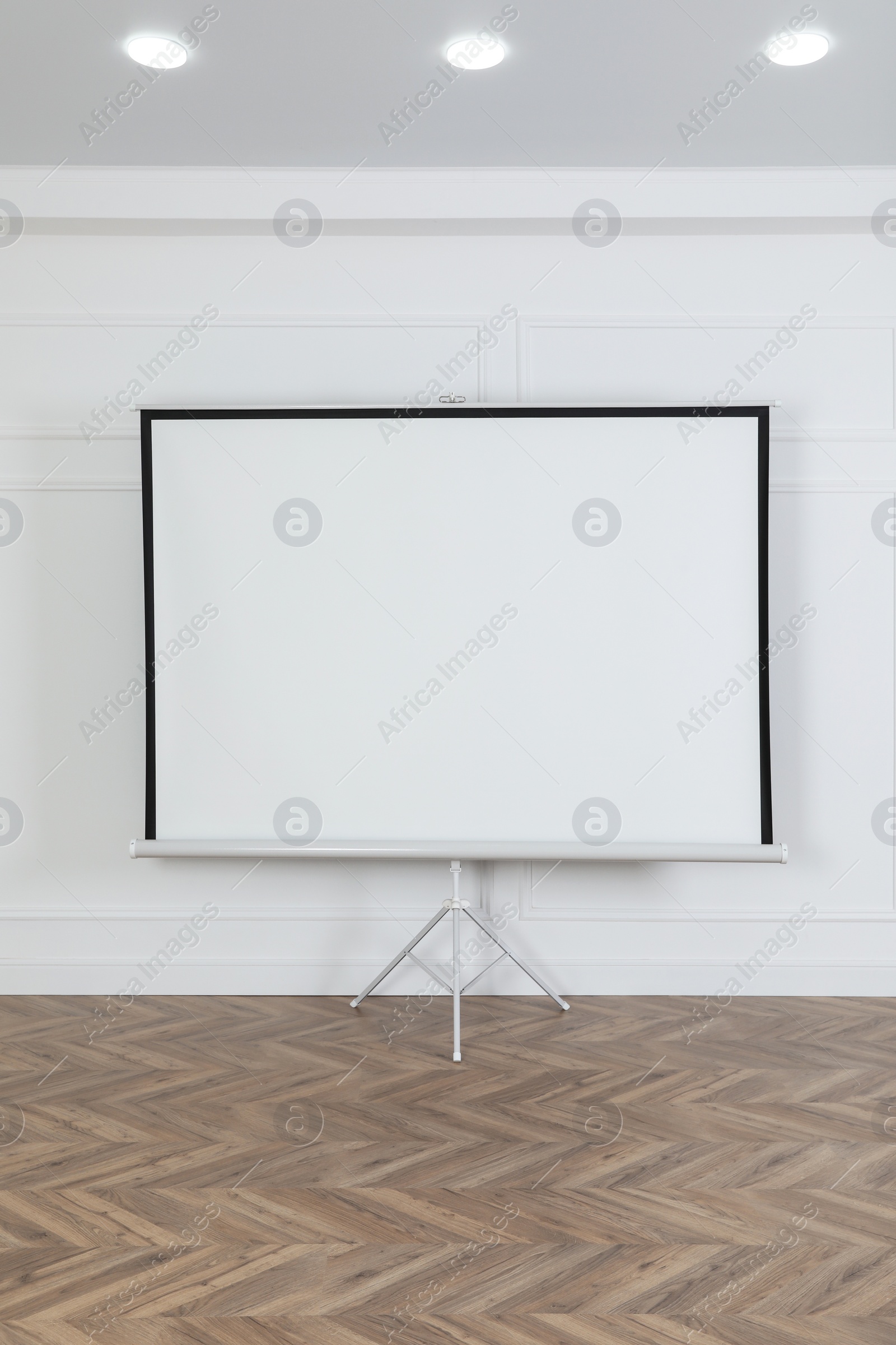 Photo of Blank projection screen near white wall indoors. Space for design