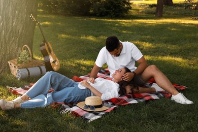 Photo of Lovely couple with guitar and picnic basket on plaid in summer park