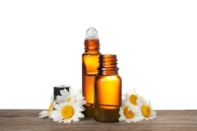 Photo of Bottles of chamomile essential oil and flowers on wooden table, white background