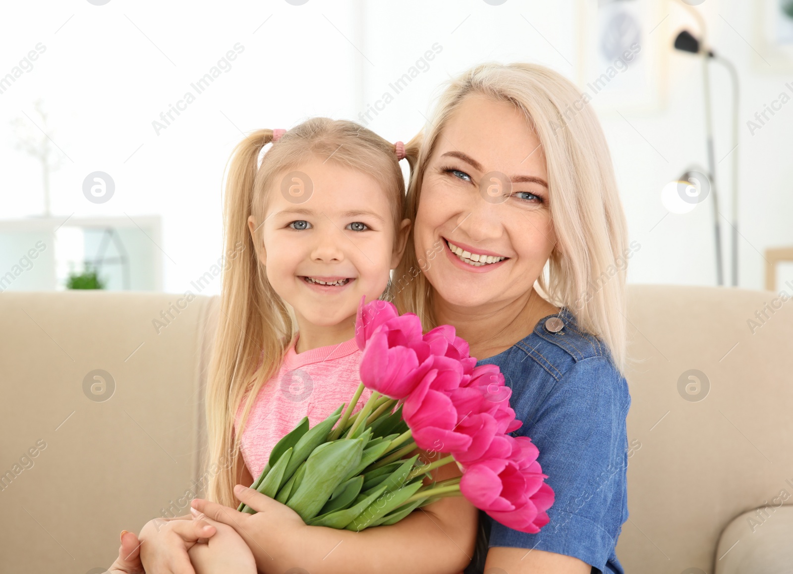 Photo of Happy little girl and her grandmother with tulip bouquet at home