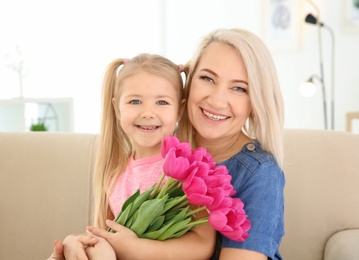 Photo of Happy little girl and her grandmother with tulip bouquet at home