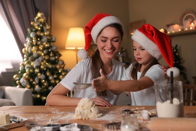 Photo of Mother with her cute little daughter making dough for Christmas cookies in kitchen