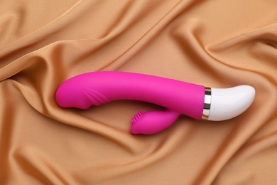 Photo of Pink vibrator on golden silk fabric, top view. Sex toy