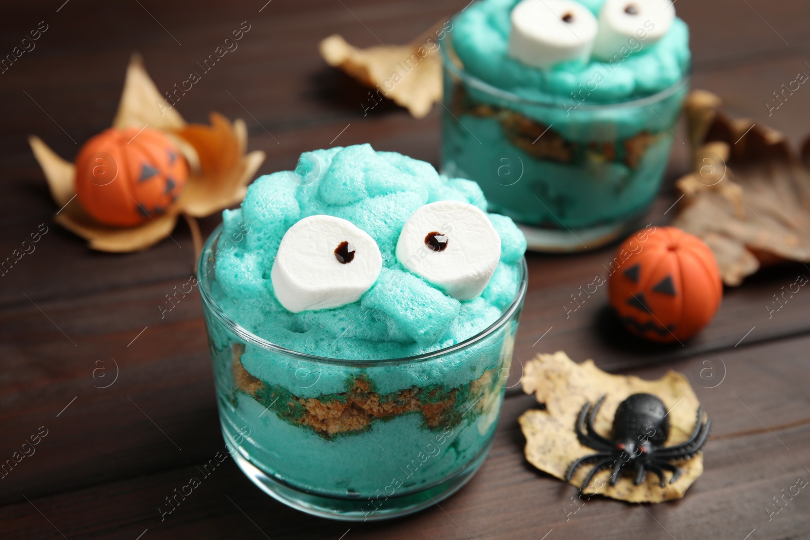 Photo of Delicious desserts decorated as monsters on wooden table, closeup. Halloween treat