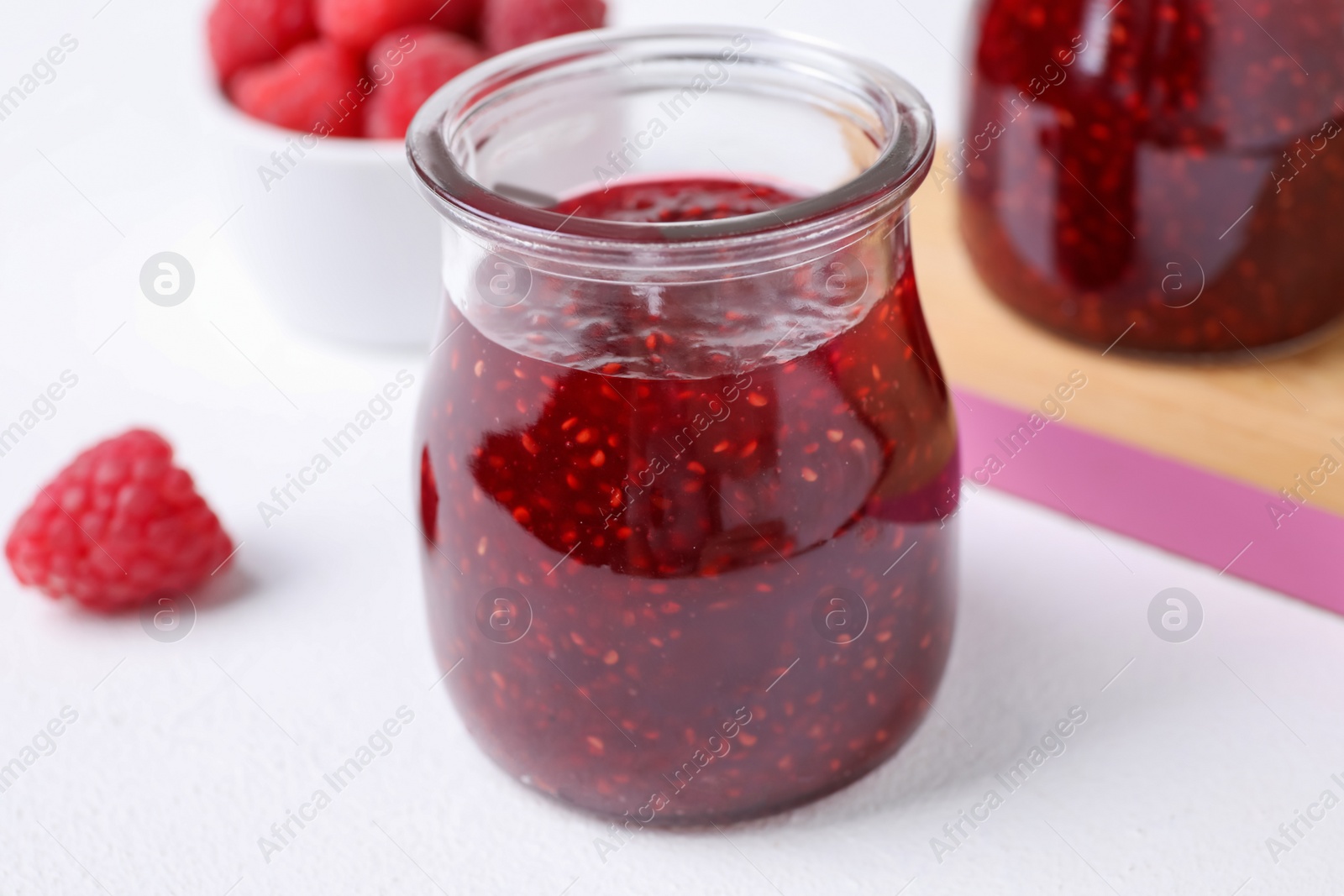 Photo of Delicious jam and fresh raspberries on white table, closeup