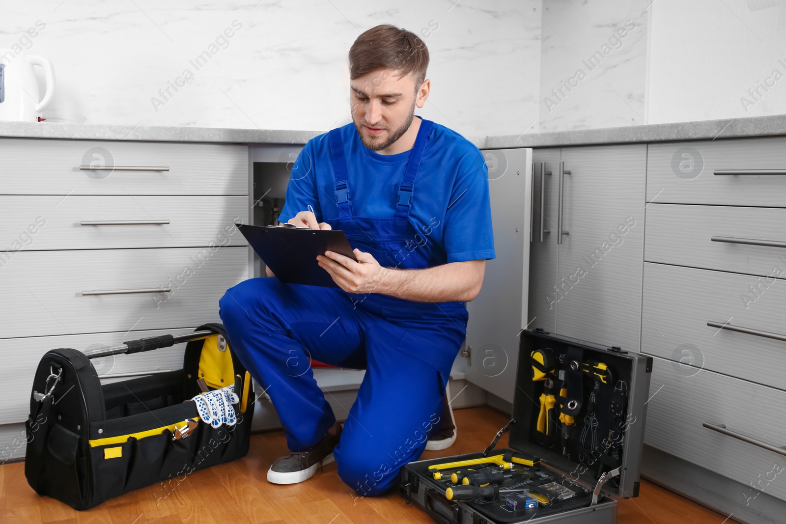 Photo of Professional plumber in uniform with clipboard near kitchen sink