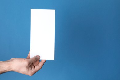 Man holding flyer on blue background, closeup. Mockup for design