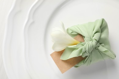 Furoshiki technique. Gift packed in green fabric with flower and blank card on plate, top view