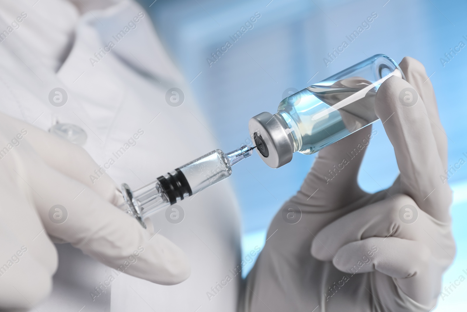 Photo of Doctor filling syringe with vaccine from vial on blurred background, closeup