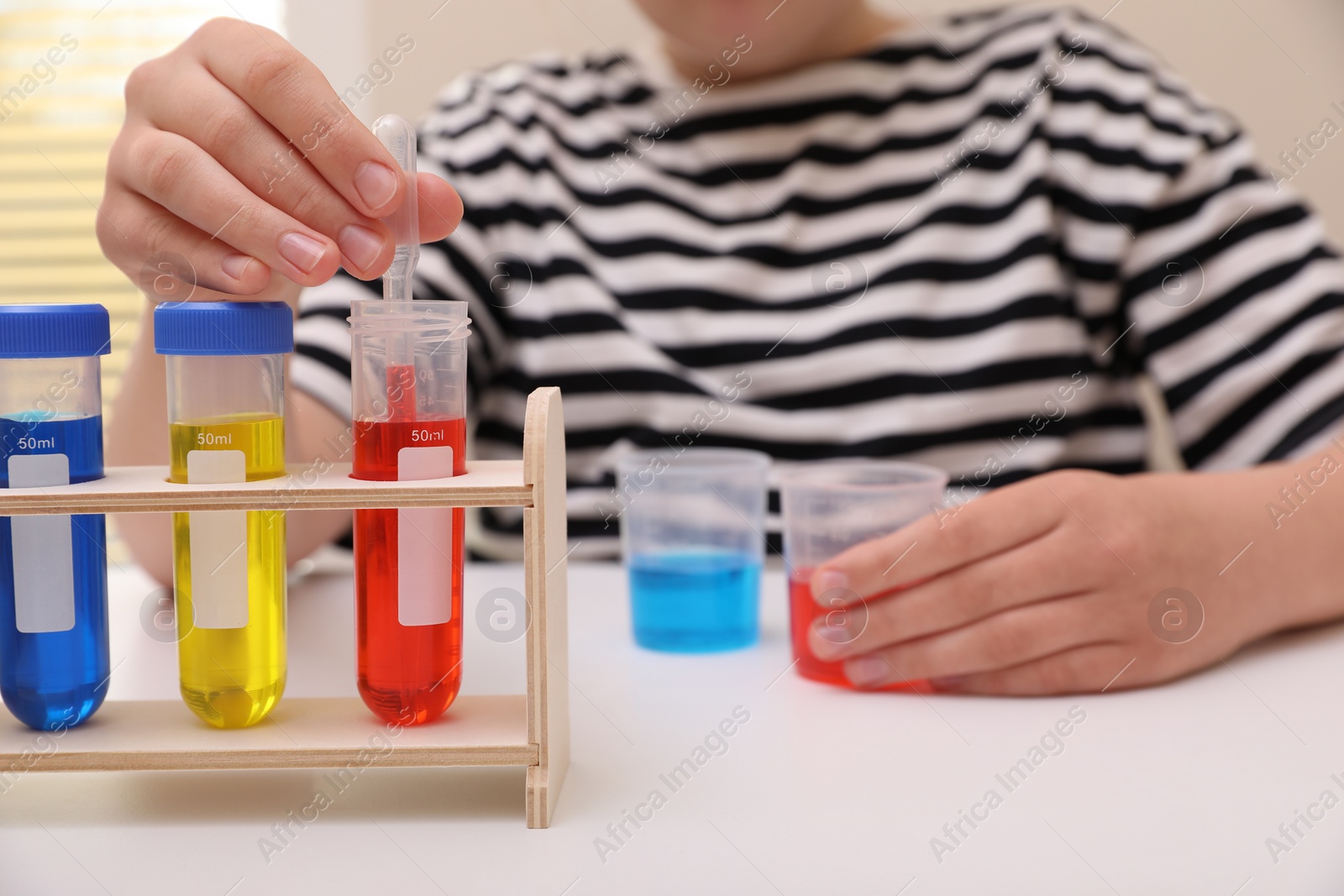 Photo of Girl mixing colorful liquids at white table indoors, selective focus. Kids chemical experiment set