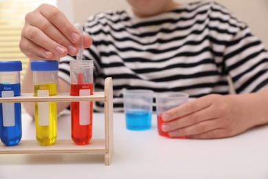 Photo of Girl mixing colorful liquids at white table indoors, selective focus. Kids chemical experiment set