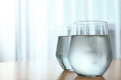 Photo of Glasses full of water on wooden table in room, space for text. Refreshing drink