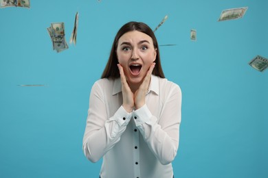 Photo of Excited woman under money shower on light blue background