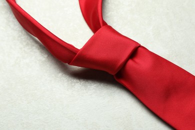Photo of One red necktie on light textured table, closeup