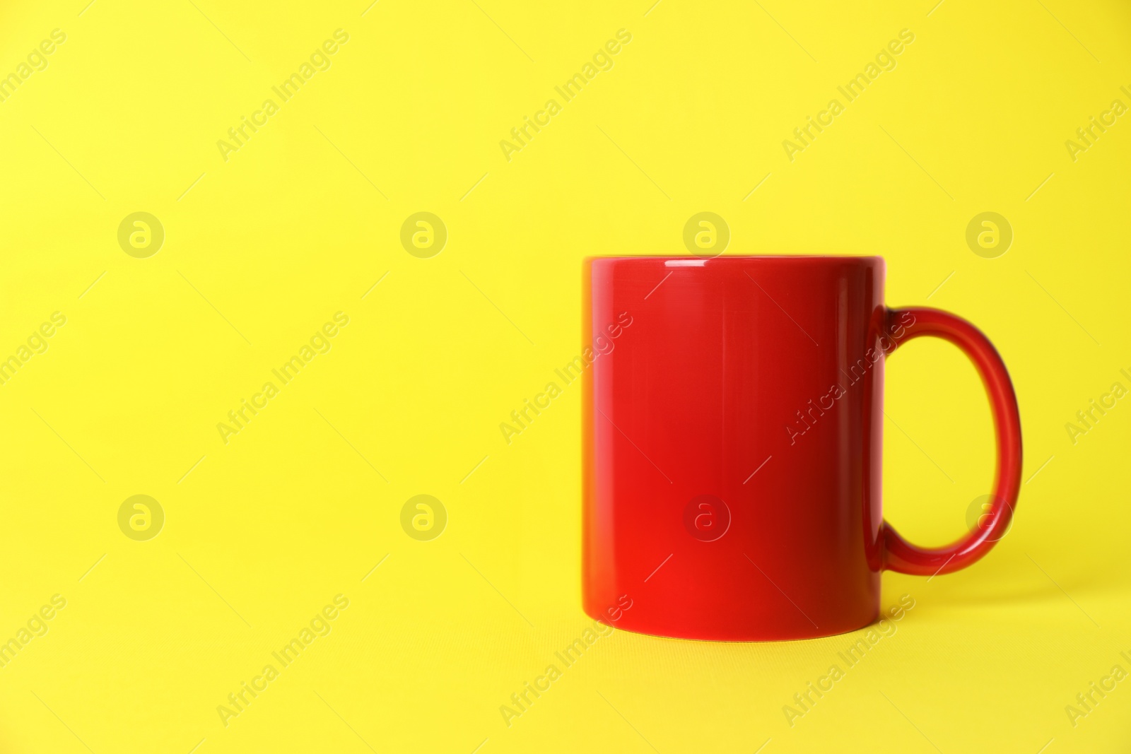 One red ceramic mug on yellow background. Space for text Photo of One red ceramic mug on yellow background. Space for text