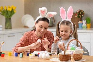 Photo of Mother and her cute daughter painting Easter eggs at table in kitchen