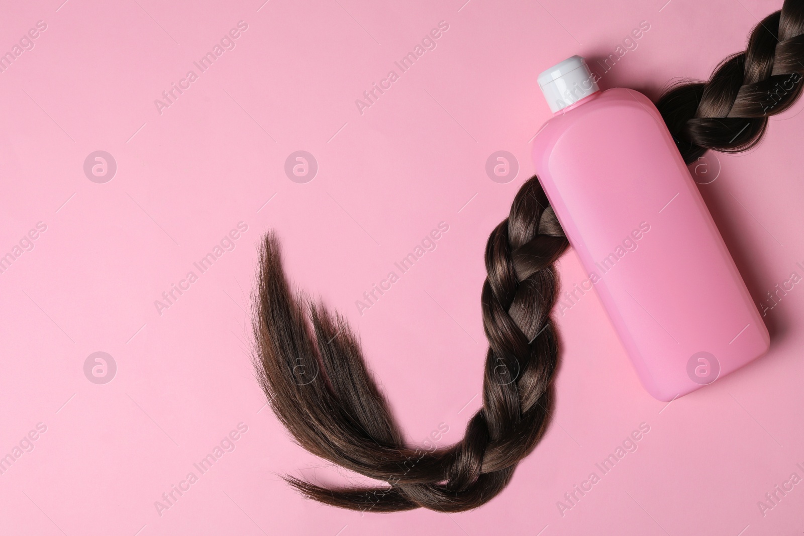 Photo of Blank bottle of cosmetic product and braided hair on pink background, flat lay. Space for design