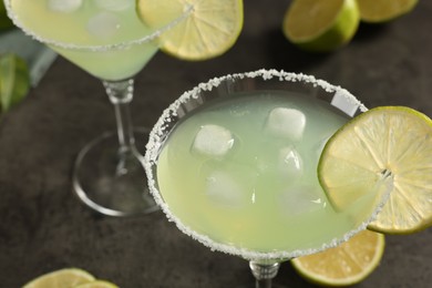 Delicious Margarita cocktail with ice cubes in glasses and lime on grey table, closeup