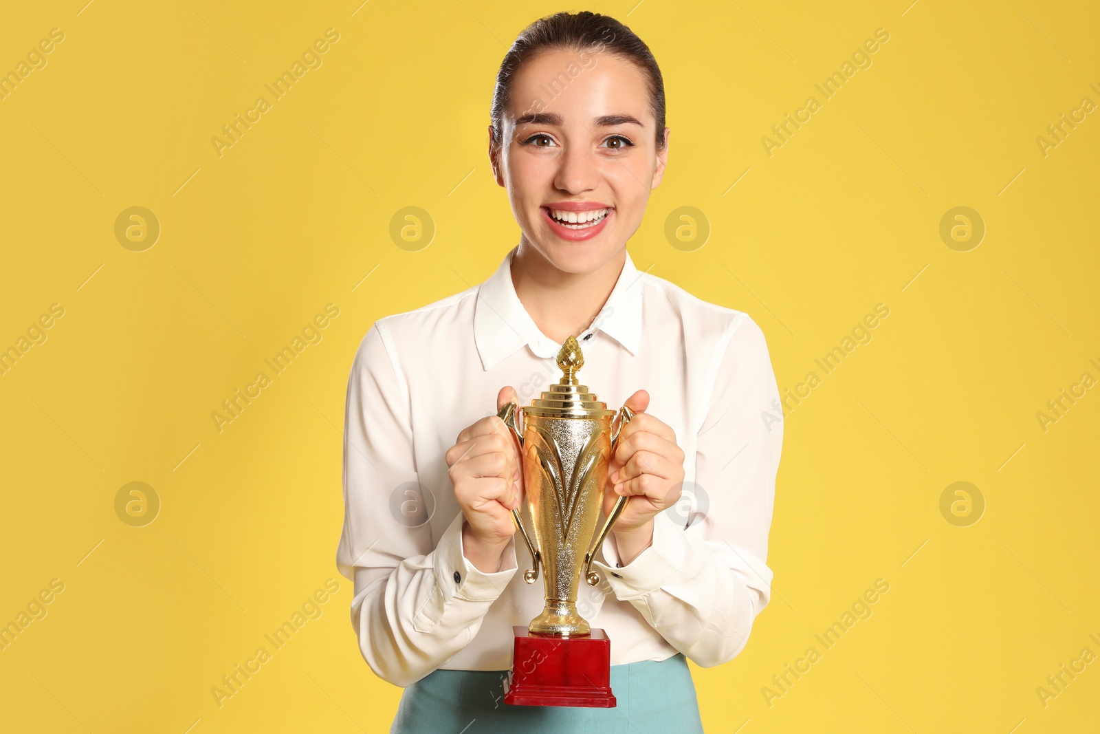 Photo of Portrait of happy young businesswoman with gold trophy cup on yellow background