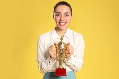 Photo of Portrait of happy young businesswoman with gold trophy cup on yellow background