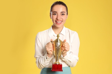 Portrait of happy young businesswoman with gold trophy cup on yellow background