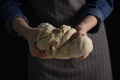 Photo of Making bread. Woman kneading dough on dark background, closeup