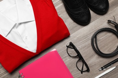 Photo of Stylish school uniform for girl, glasses and stationery on wooden background, flat lay