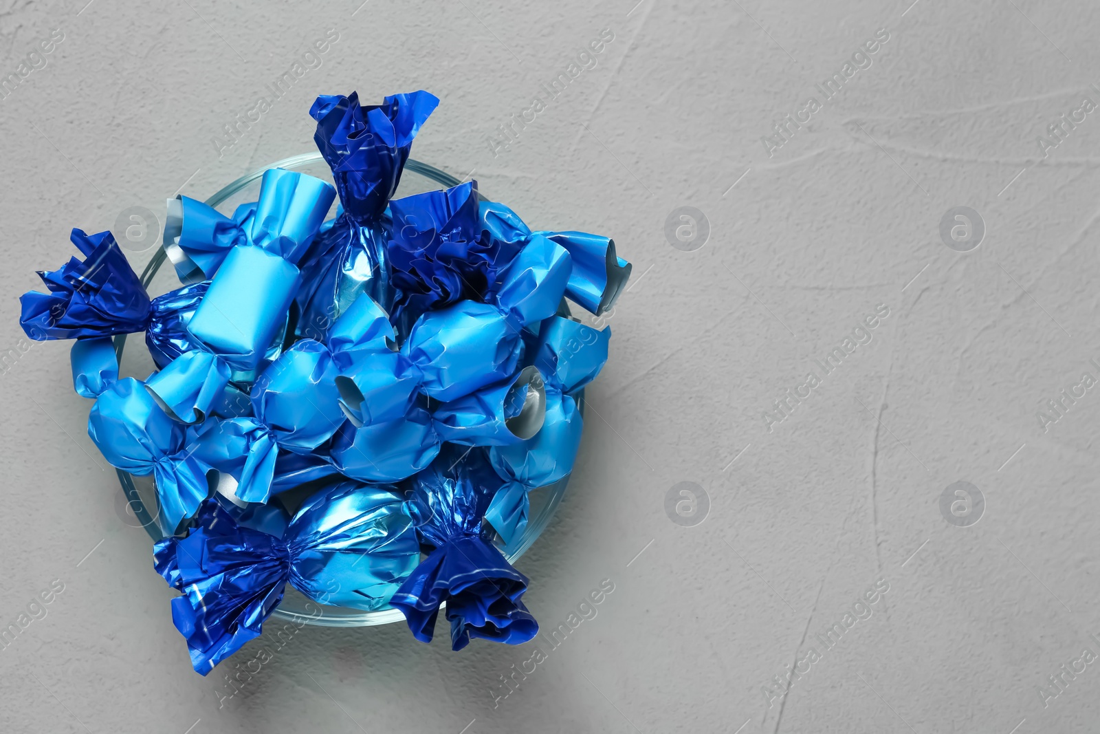 Photo of Candies in blue wrappers on grey table, top view. Space for text