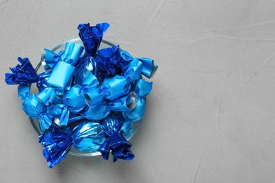 Candies in blue wrappers on grey table, top view. Space for text