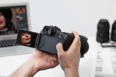 Photo of Professional photographer with digital camera at table indoors, closeup