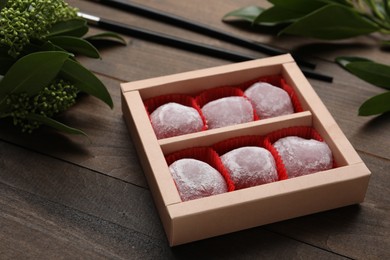 Photo of Box of delicious mochi and leaves on wooden table. Traditional Japanese dessert
