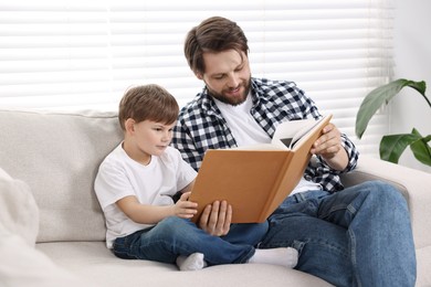 Photo of Dad and son reading book together on sofa at home