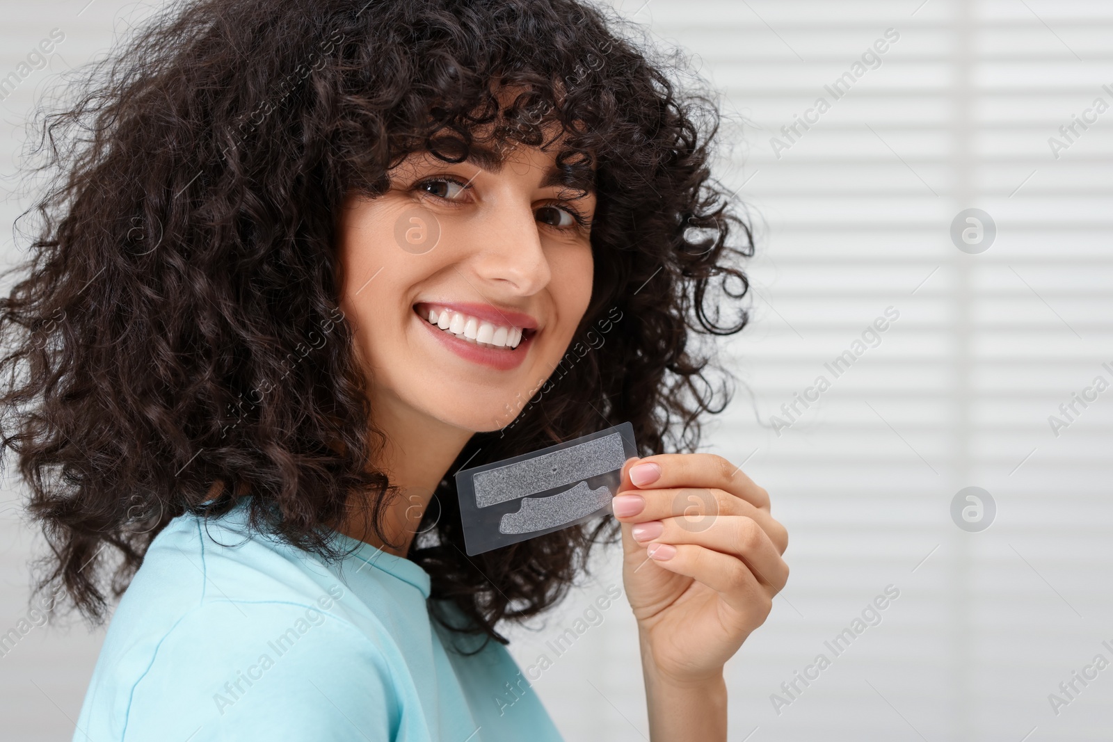 Photo of Young woman holding teeth whitening strips indoors, space for text