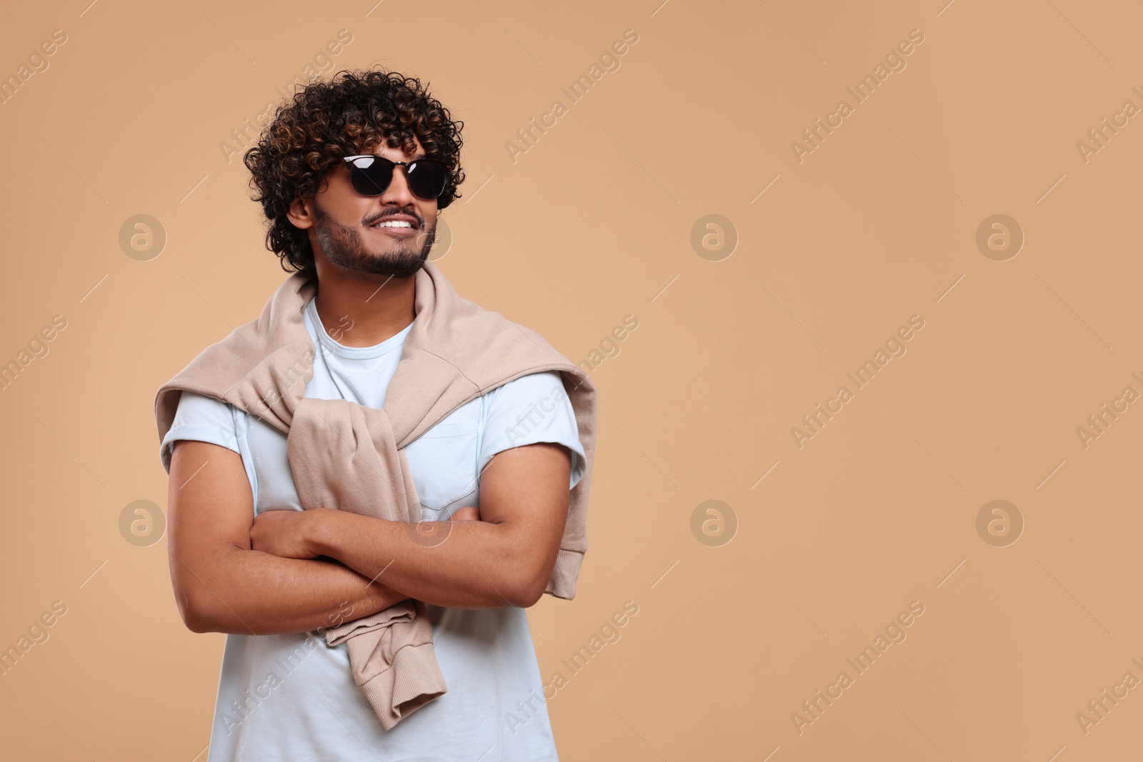 Photo of Handsome young smiling man in sunglasses on beige background, space for text