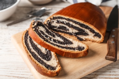 Photo of Cut tasty sweet bun with poppy seeds on wooden table