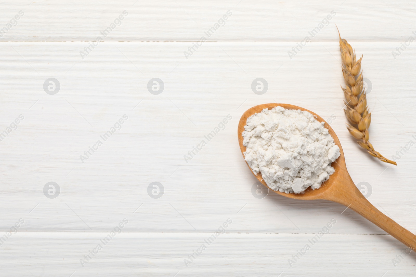 Photo of Spoon of wheat flour on white wooden table, flat lay. Space for text