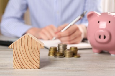 Woman planning budget at wooden table, focus on house model